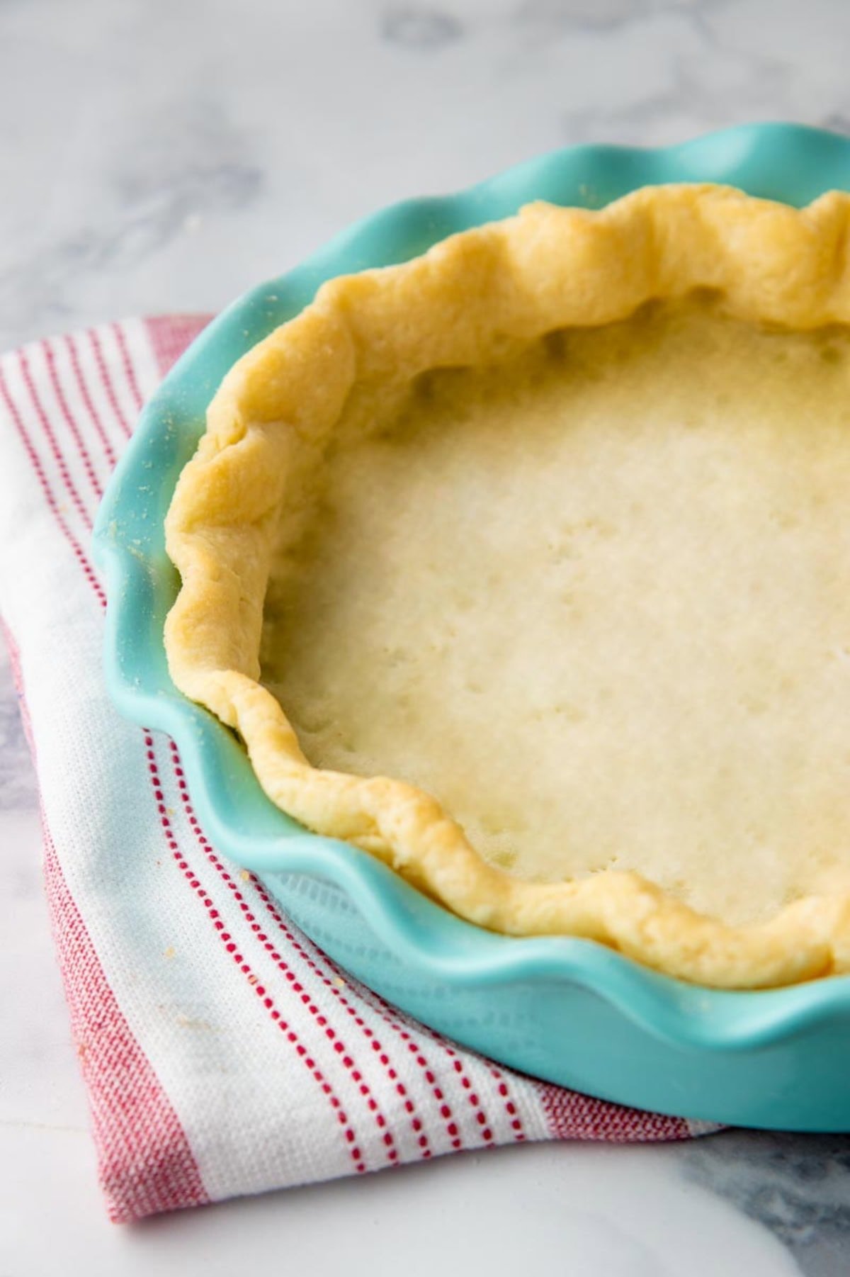 A blind-baked gluten-free pie crust in a teal pie plate on top of a striped towel.