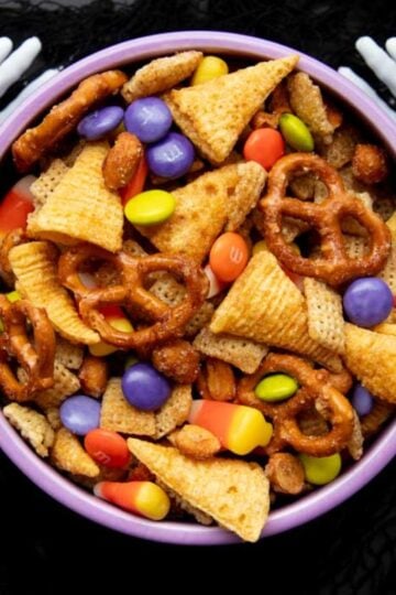 Fake skeleton hands hold a bowl of Halloween Chex Mix