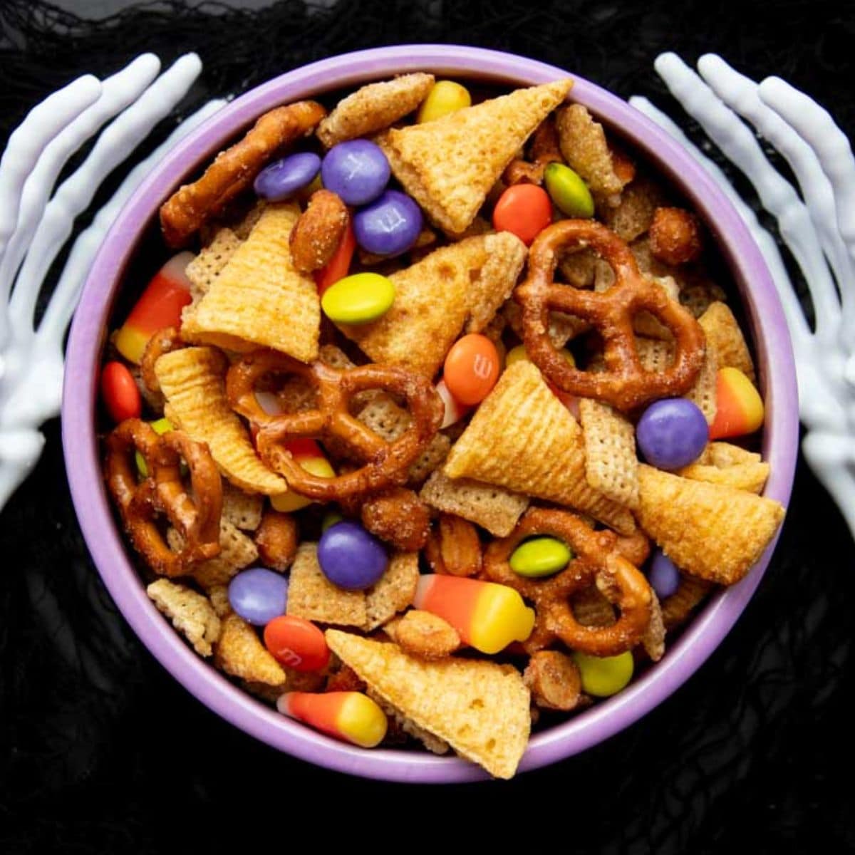 Fake skeleton hands hold a bowl of Halloween Chex Mix