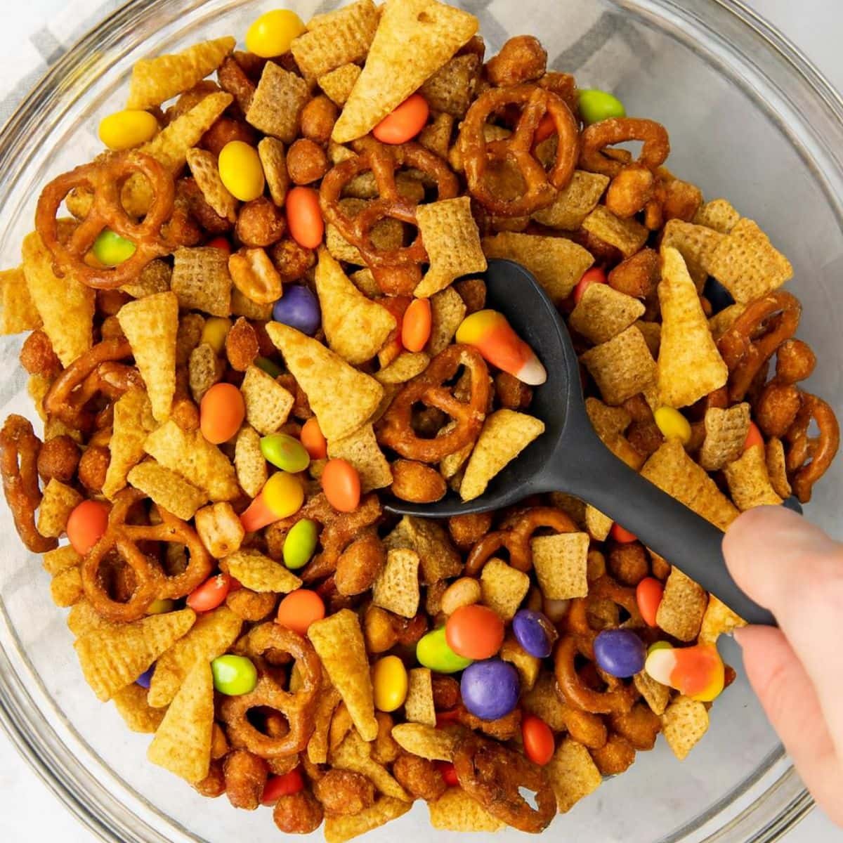 Black spoon stirs candy into cereal, chips, and pretzels