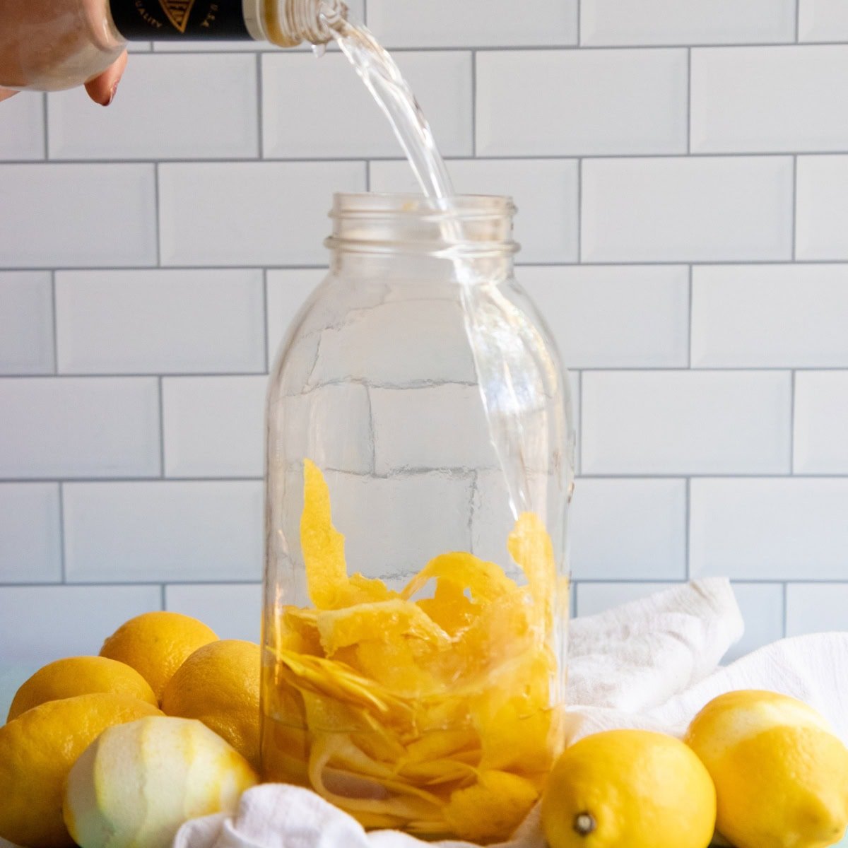 Everclear pours into a large jar of lemon peels for homemade limoncello.