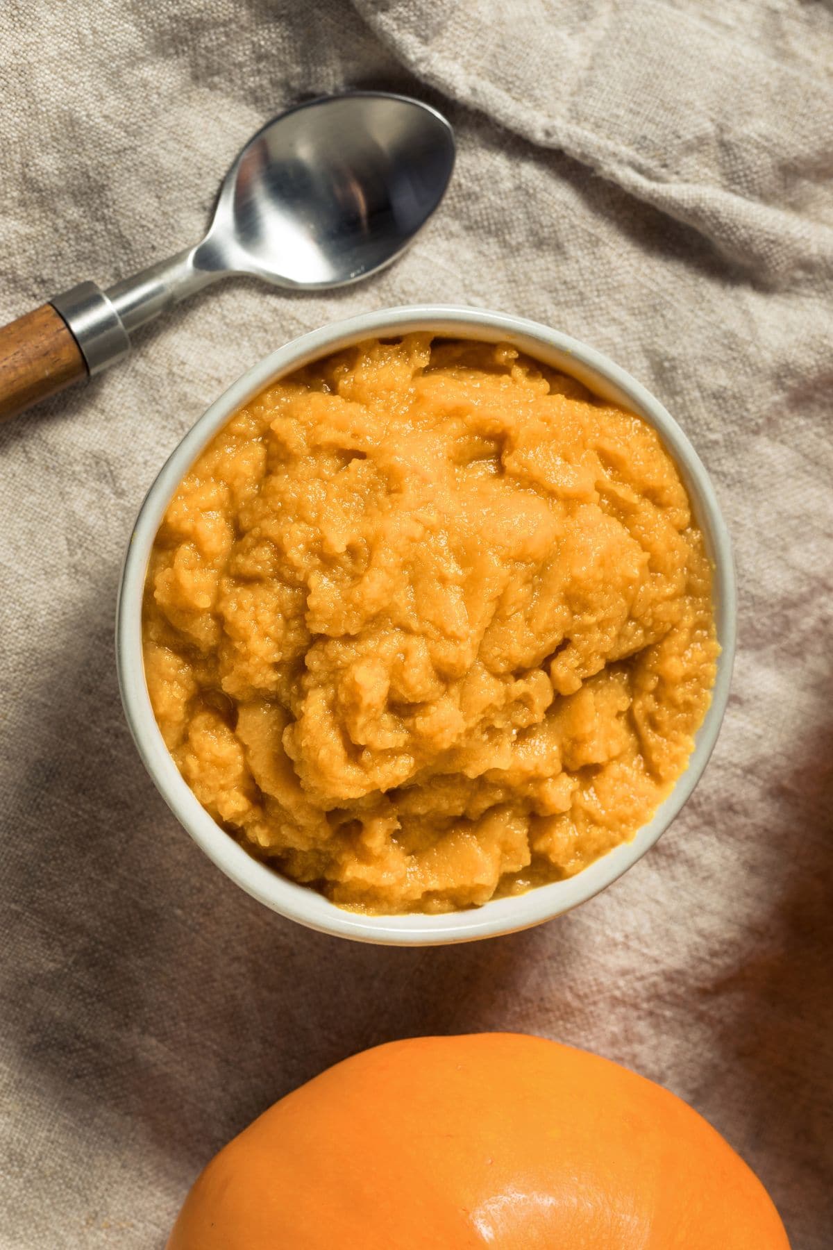 Yellow-orange puree in a white bowl next to a spoon.