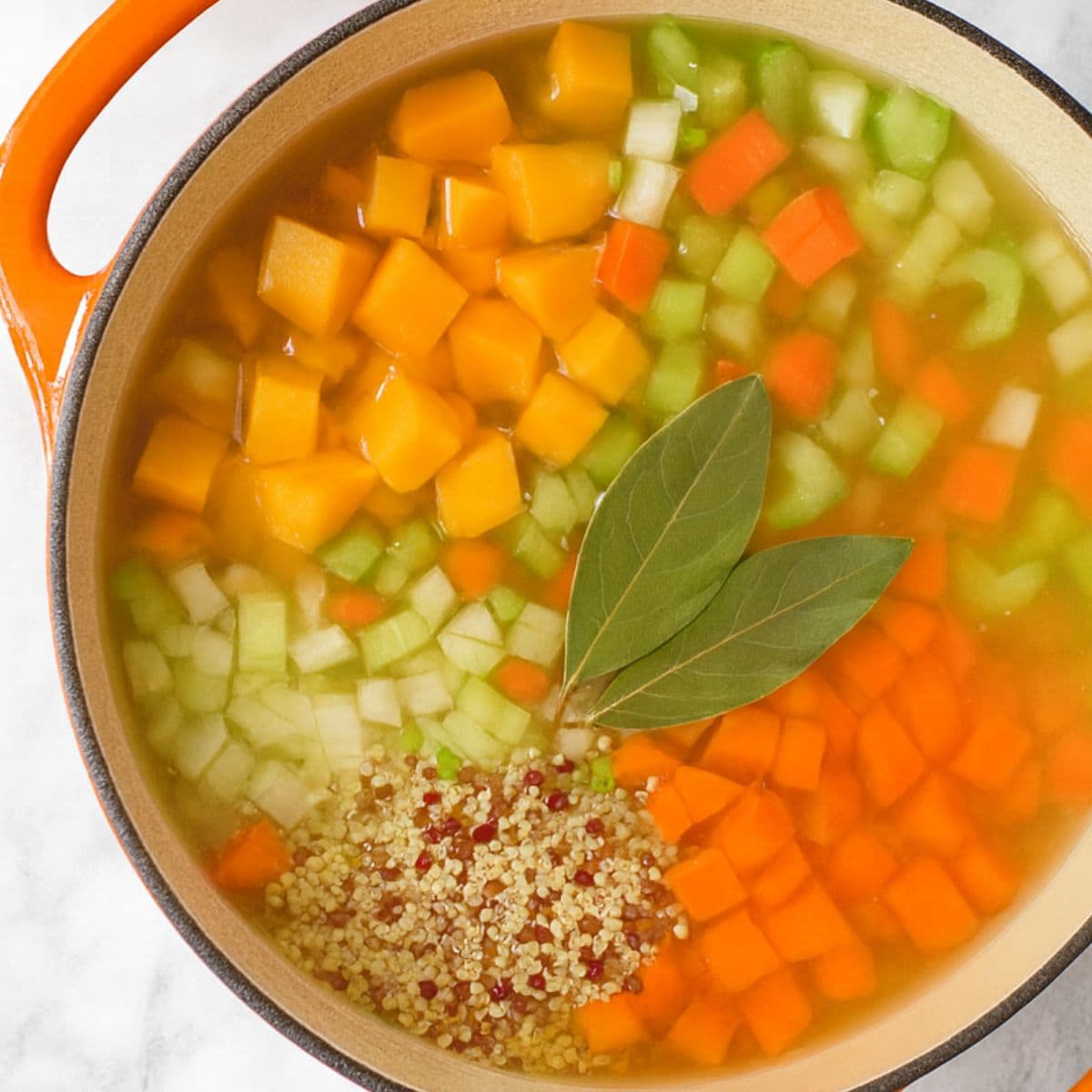 A soup pot filled with chopped vegetables, quinoa, and broth.