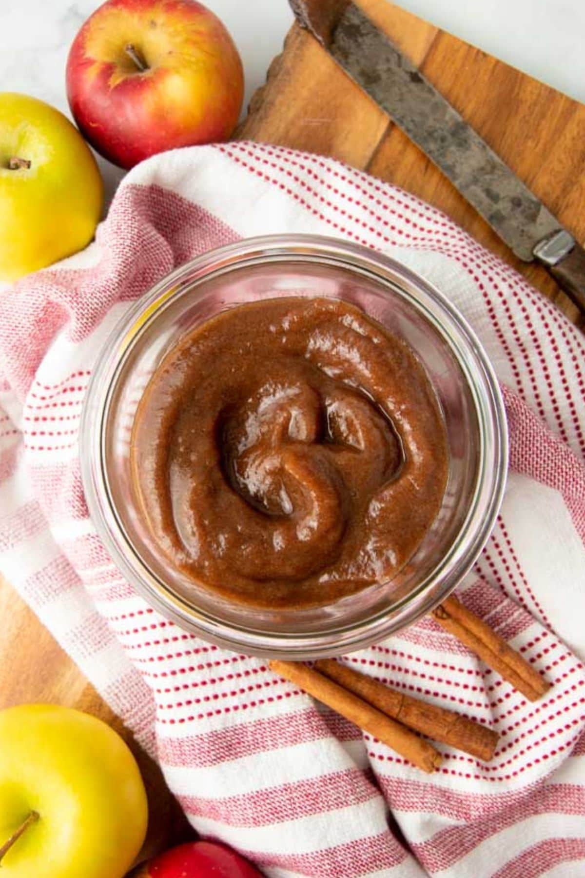 Apple butter in a glass jar surrounded by apples