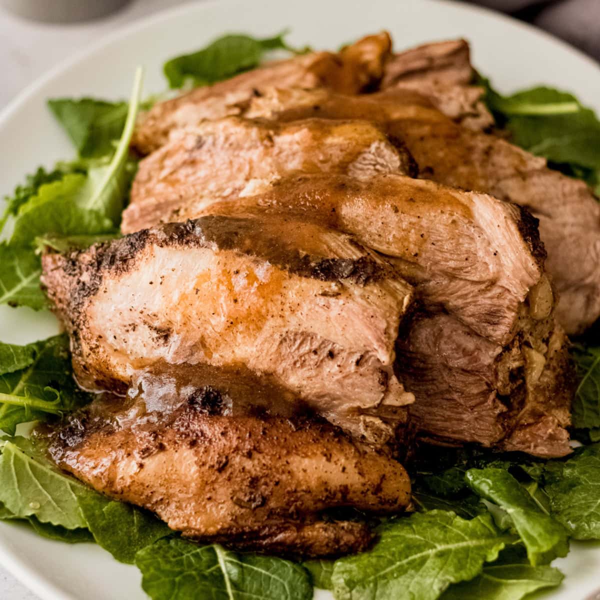 Sliced Instant Pot pork roast with sauce on a bed of greens.