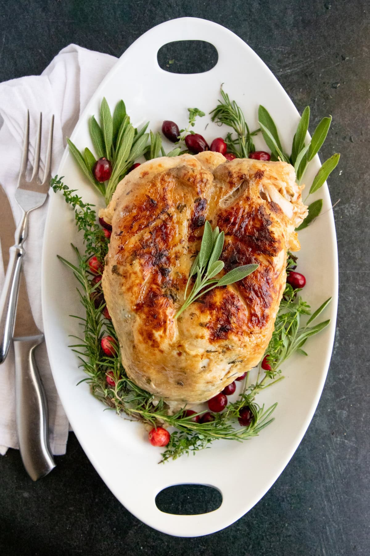 Instant Pot turkey breast on a bed of fresh herbs on a white oval platter.