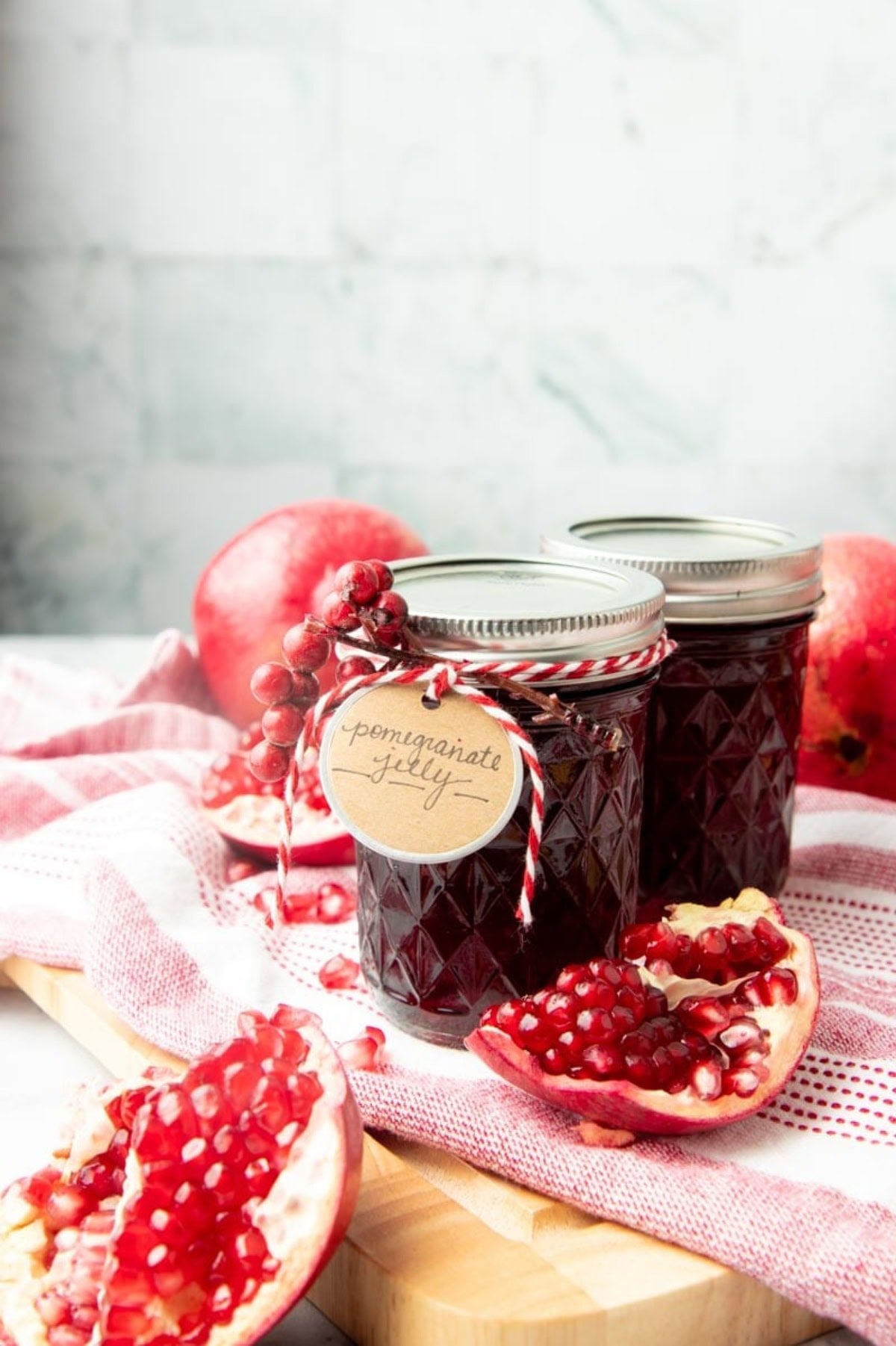 Two jars of pomegranate jelly surrounded by pomegranates, one split to show the arils inside.
