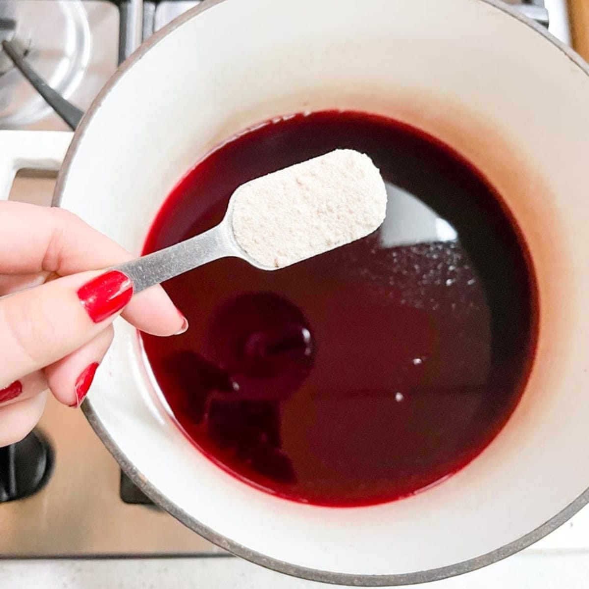 A hand adds pectin to pomegranate jelly.
