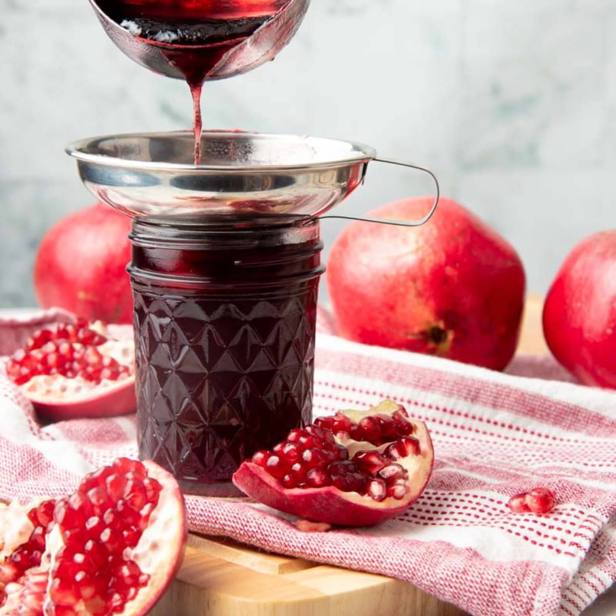 A ladle pours pomegranate jelly through a metal funnel into a mason jar.