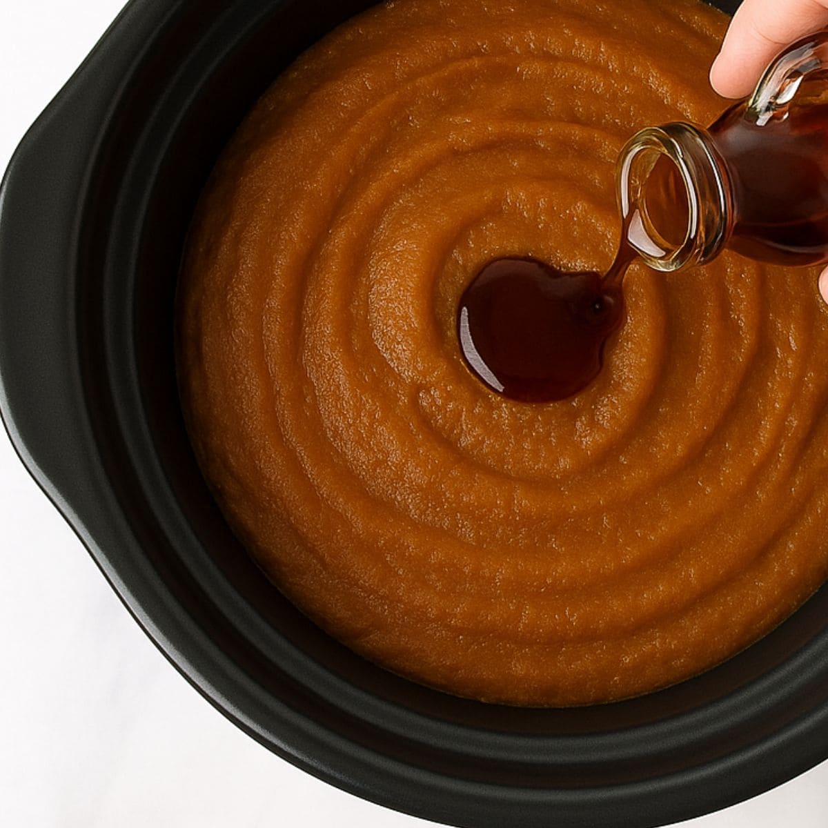 Maple syrup pours into a slow cooker filled with pumpkin butter