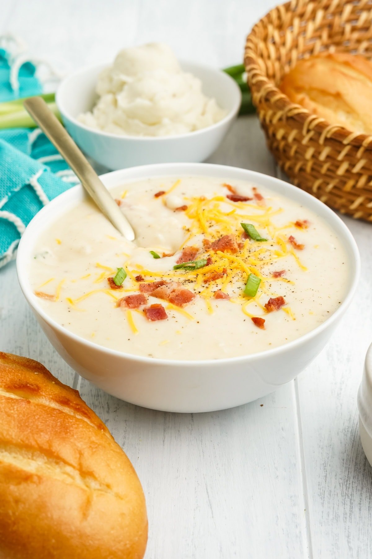 A bowl of mashed potato soup next to a loaf of bread.