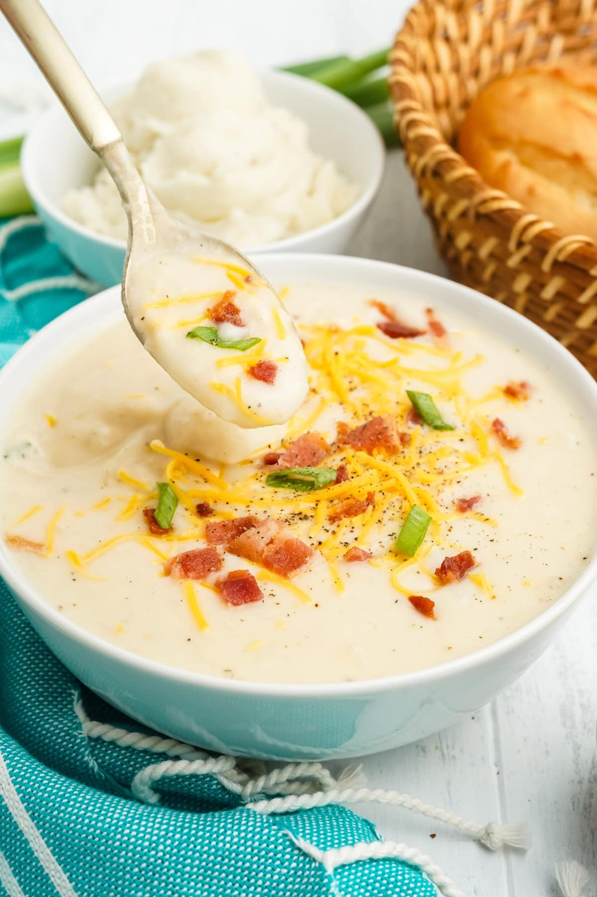 A spoon holds a bite of potato soup with mashed potatoes over a bowl of soup.