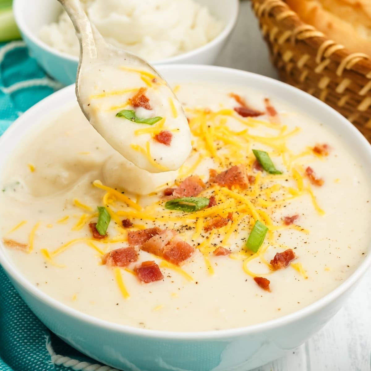 A spoonful of soup held over a bowl of mashed potato soup.
