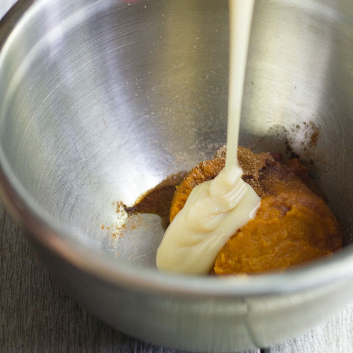 Sweetened condensed milk streams into a bowl containing pumpkin and spices