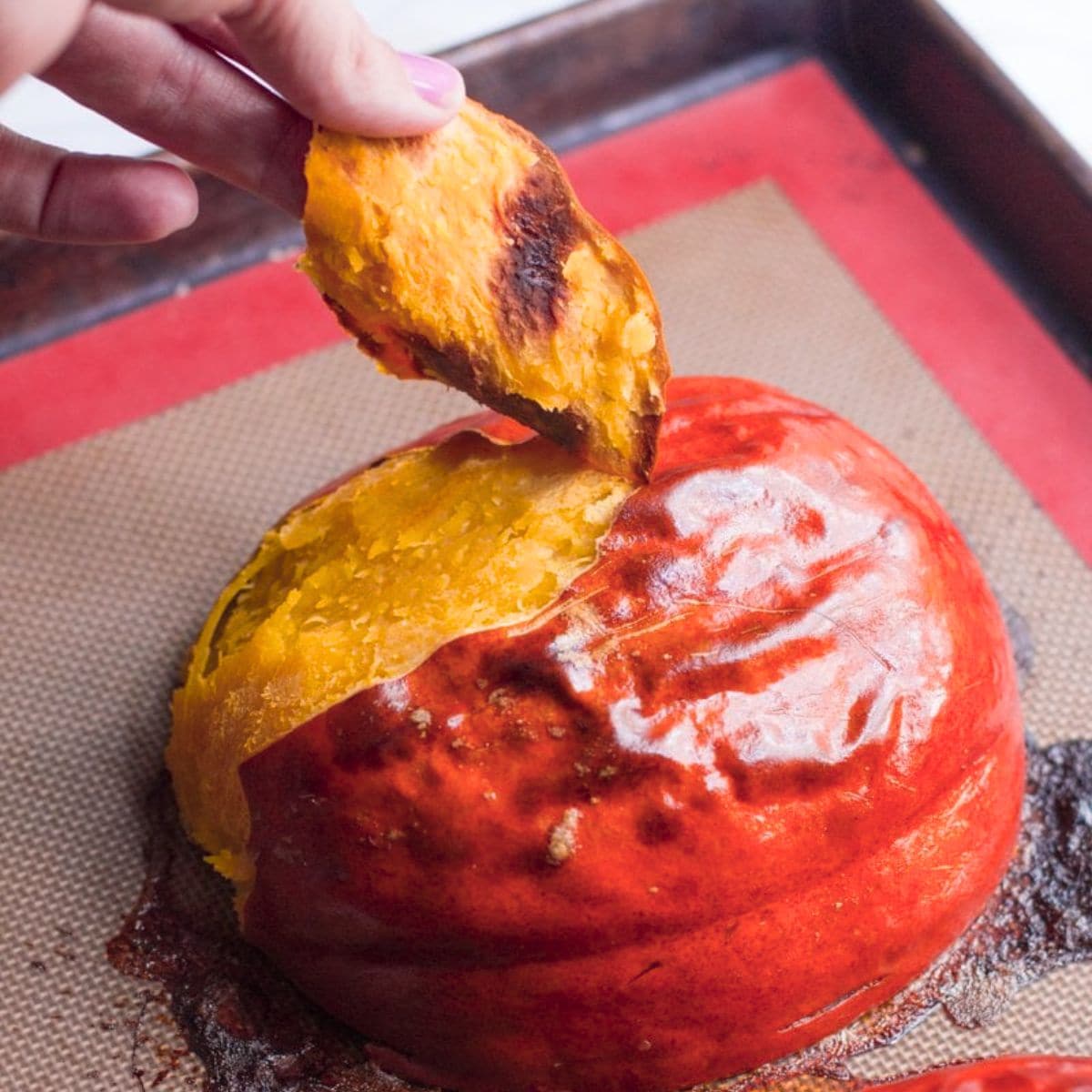 A hand peels the skin off a roasted pumpkin half.
