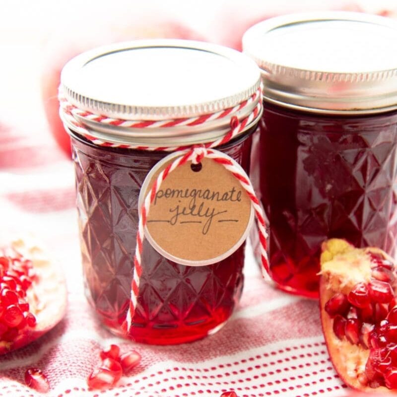 Two jars of pomegranate jelly, one wrapped in bakers' twine and a round tag.