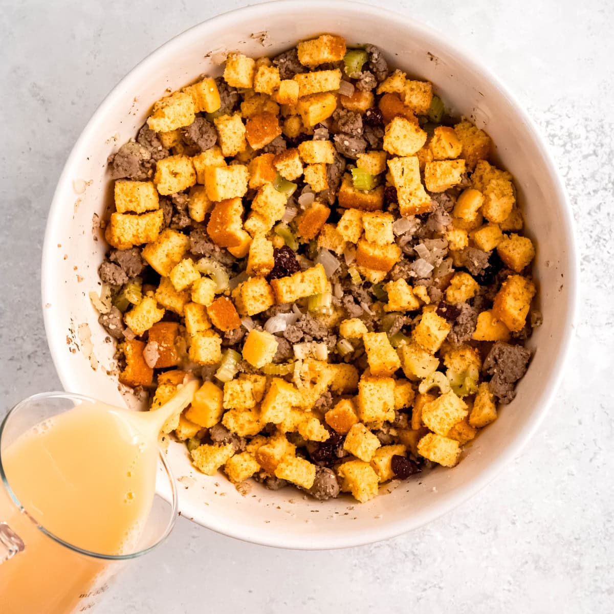 Broth pours over a bowl of cornbread, cooked sausage, and sauteed onions.