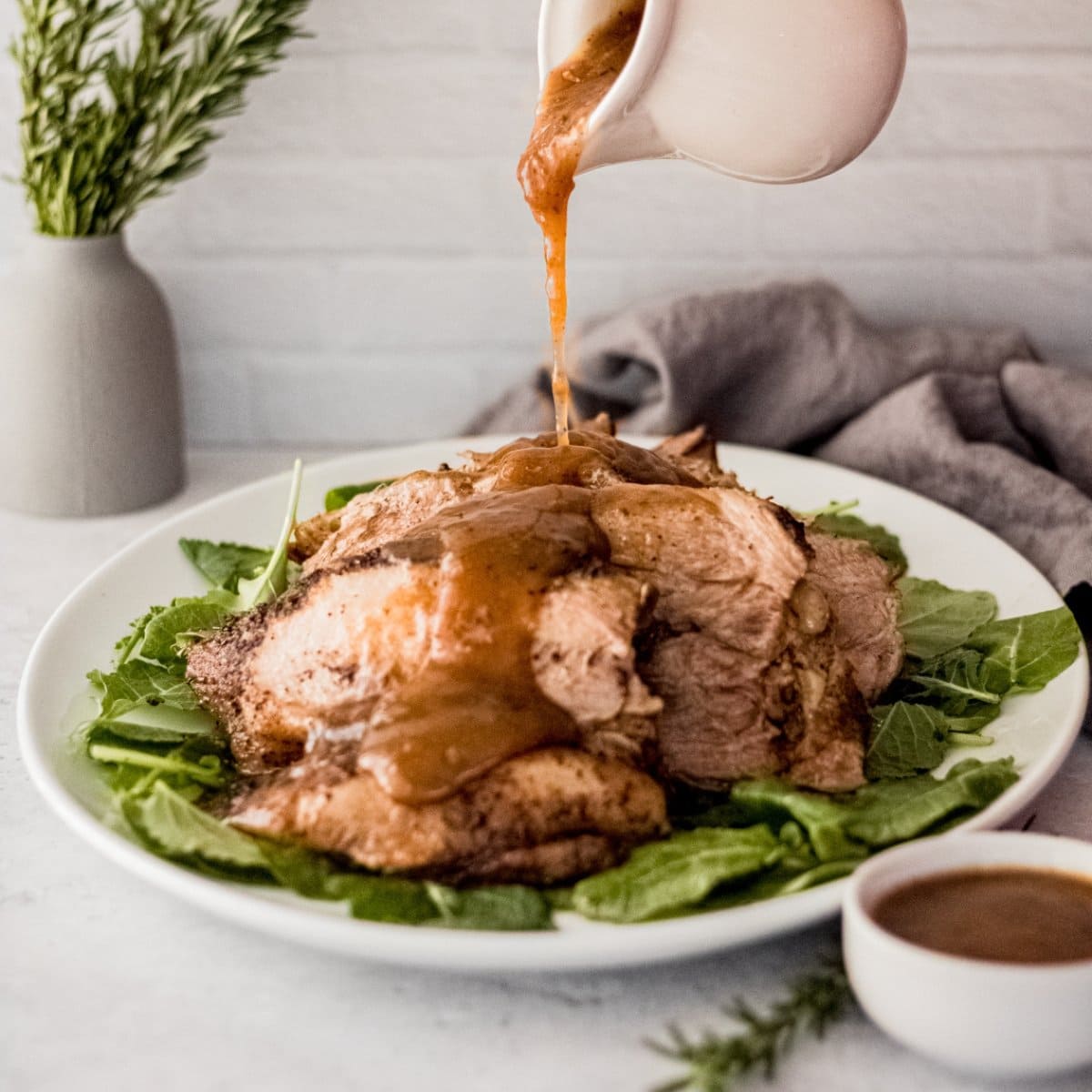 A gravy boat pours sauce over an Instant Pot pork roast.