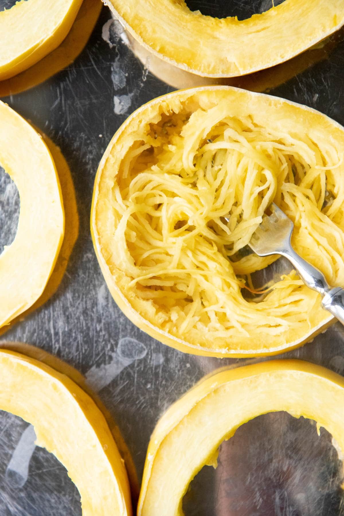 A fork pulls spaghetti squash noodles out of a ring of roasted squash