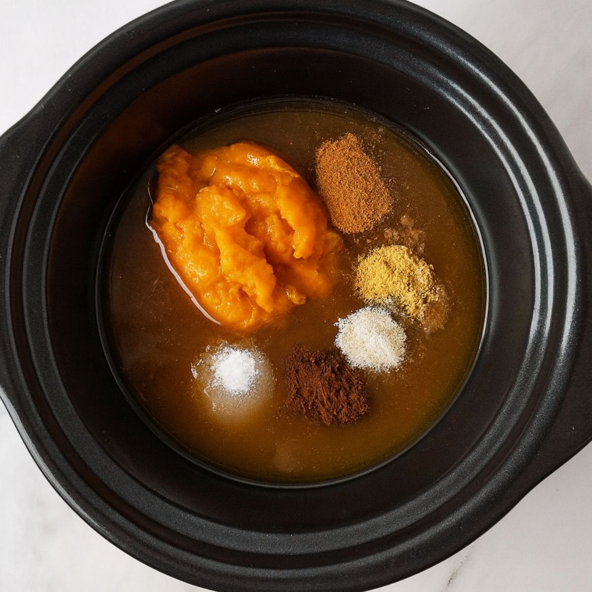 Pumpkin, spices, and apple cider in the basin of a slow cooker