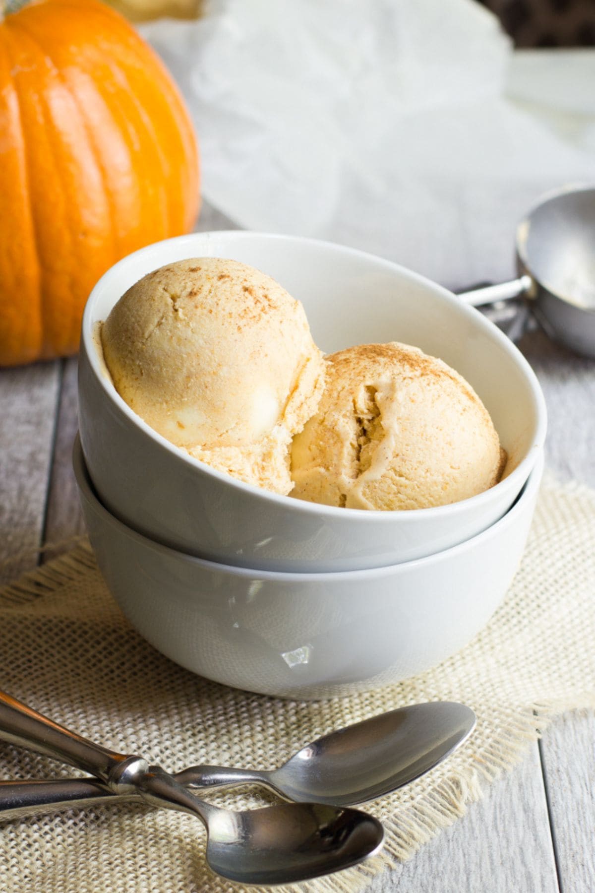Two scoops of pumpkin ice cream in a white bowl in front of a fresh pumpkin
