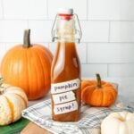 Bottle of homemade pumpkin spice syrup surrounded by mini pumpkins