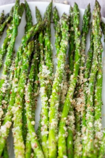 Roasted asparagus sprinkled with Parmesan on a white plate.