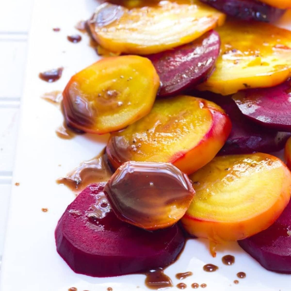 Red and golden beets with balsamic glaze on a white plate.