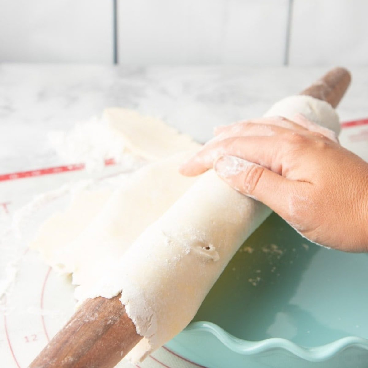 Hands drape a gluten-free pie crust over a rolling pin to transfer it to the pie pan.