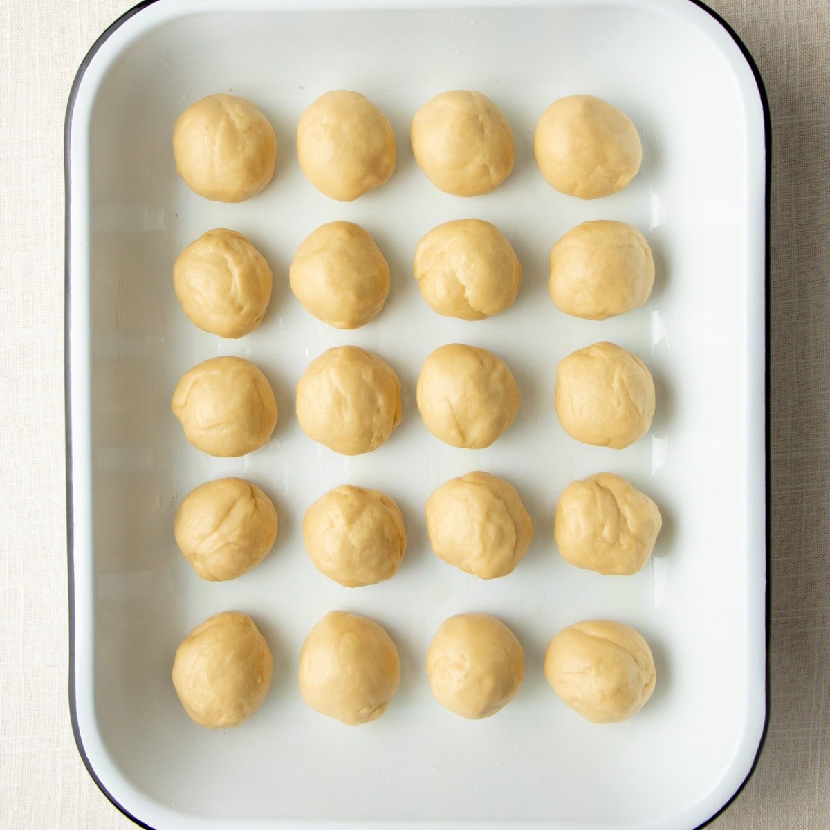 Balls of bread dough in a baking dish, before rising.