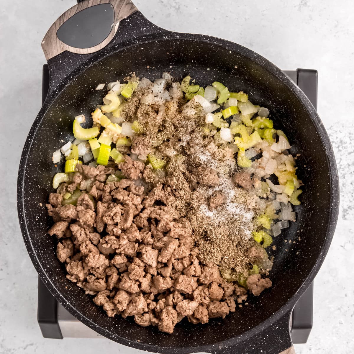 Ground turkey, celery, onions, and herbs cooking in a pan.