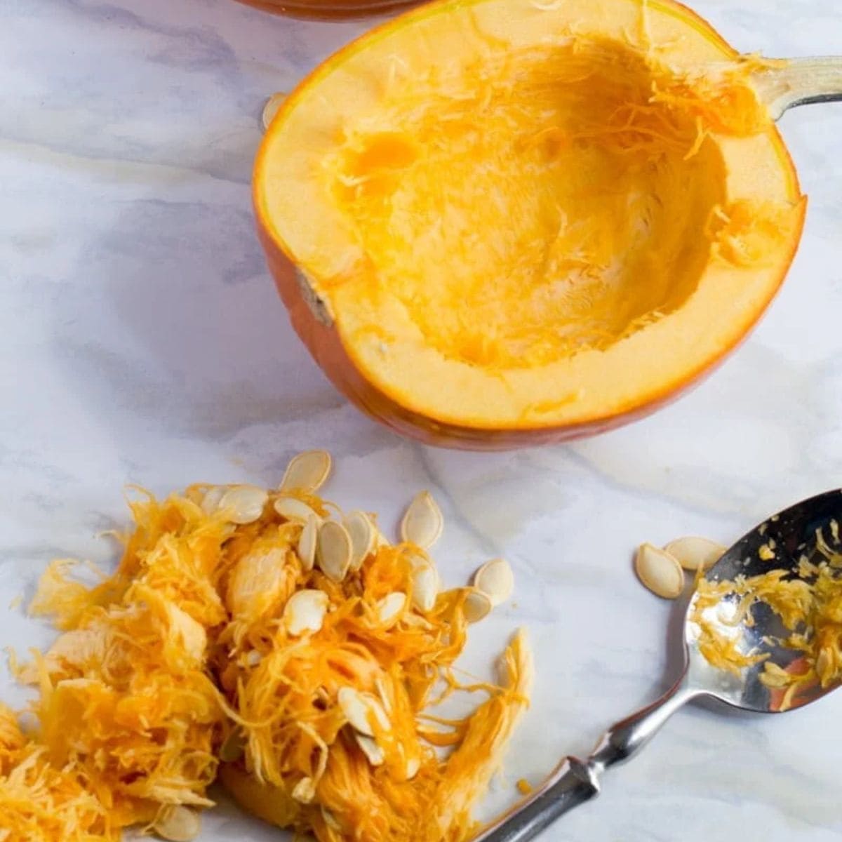 Half of a pumpkin with the "guts" scooped out. A spoon and the stringy innards of the pumpkin are next to it.