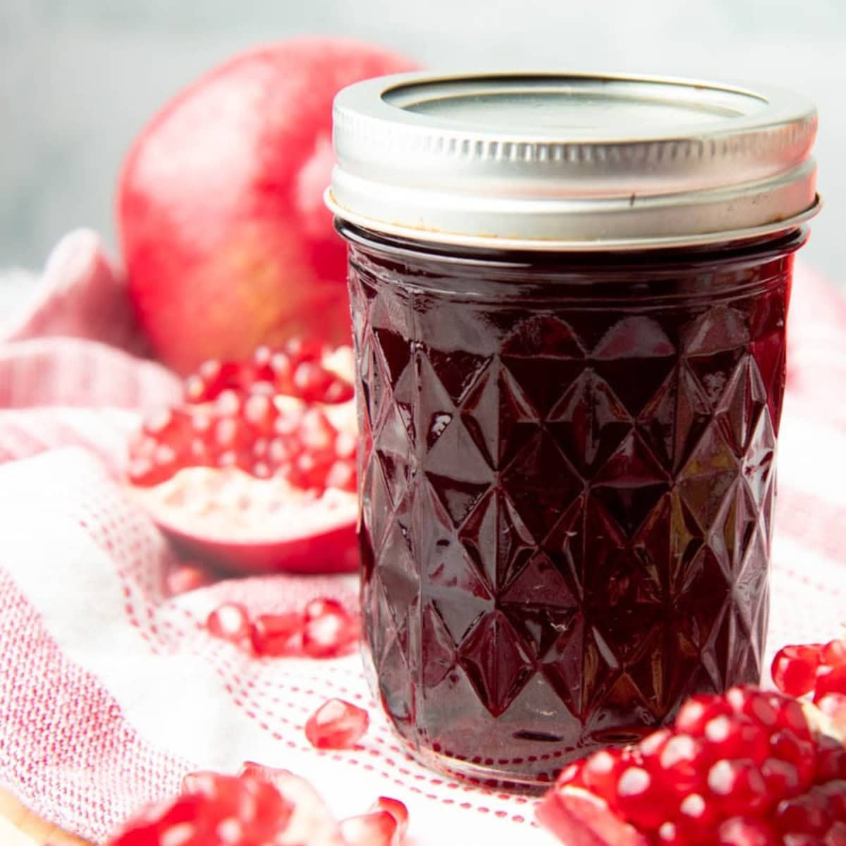A jar of pomegranate jelly surrounded by pomegranates.
