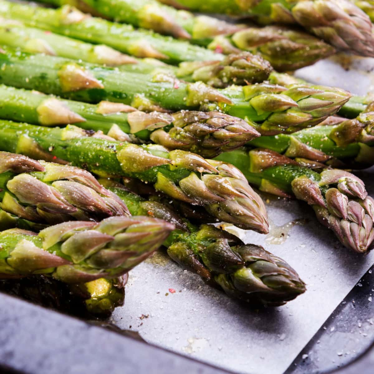 Seasoned and oiled asparagus on a baking sheet lined with parchment paper.