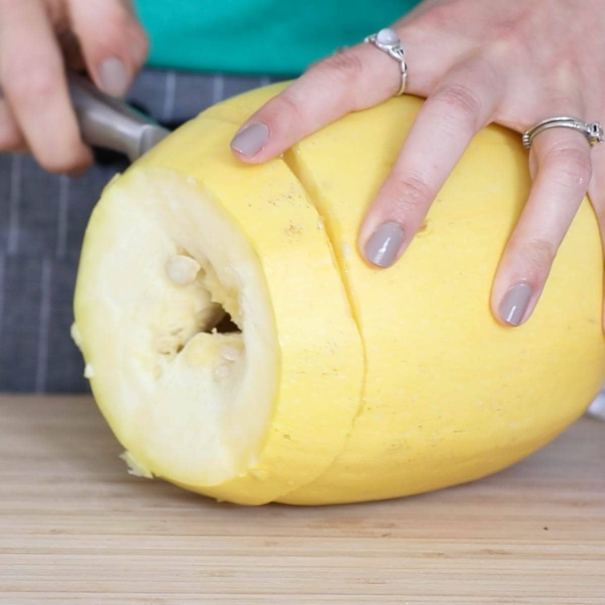 One hand holds a spaghetti squash stable while the other slices into it crosswise.