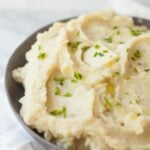 Slow cooker mashed potatoes in a gray bowl, topped with a pat of butter and chopped chives.