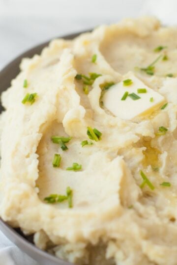 Slow cooker mashed potatoes in a gray bowl, topped with a pat of butter and chopped chives.