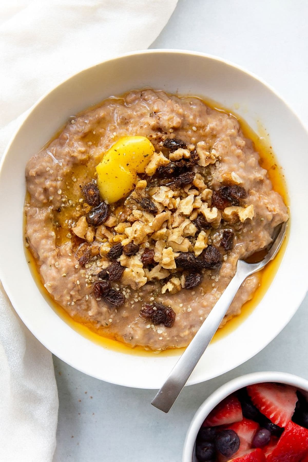 A white bowl of steel cut oats topped with ghee, raisins, and nuts.