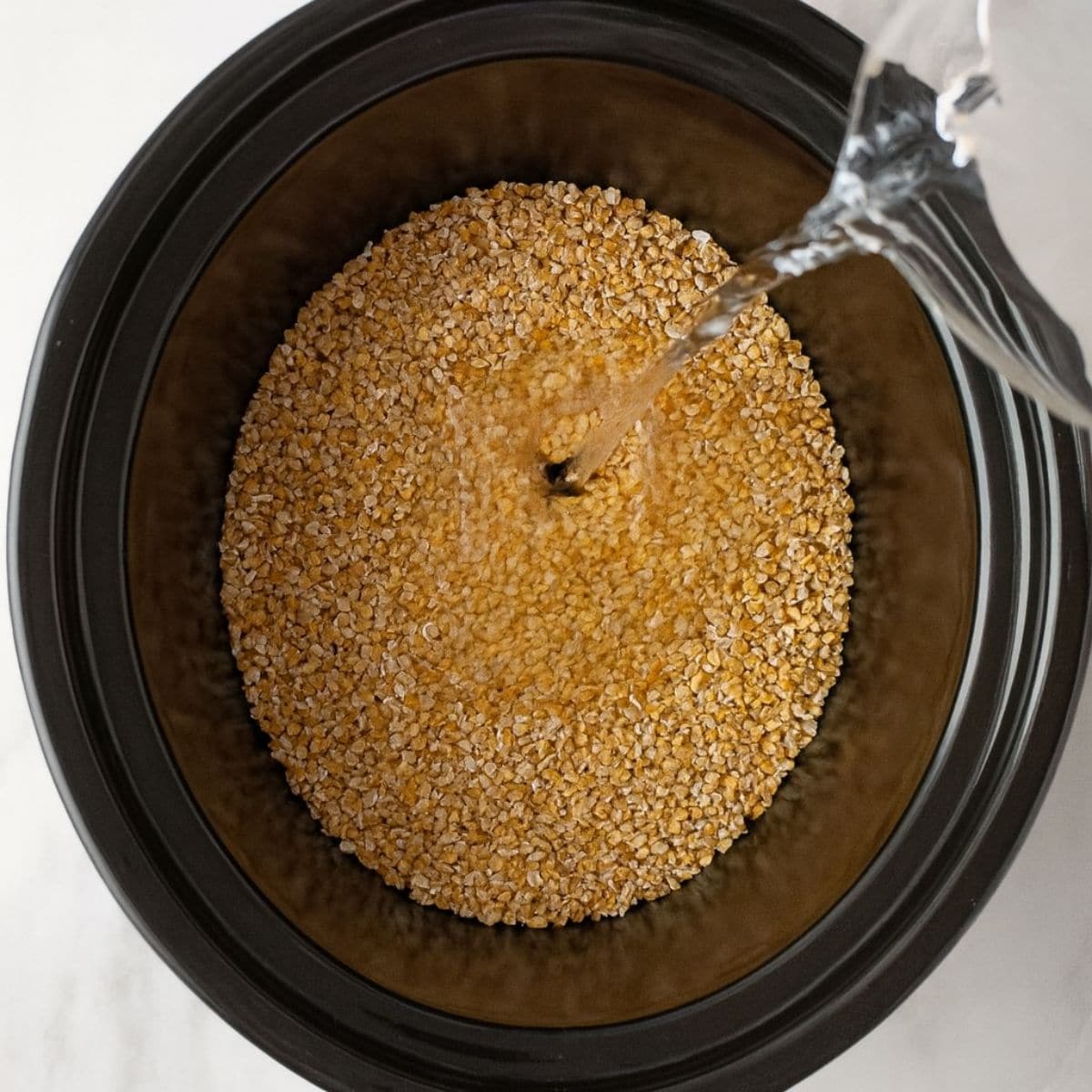 Water pours over steel cut oats in the basin of a slow cooker.