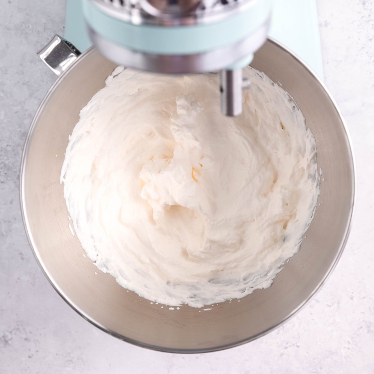 Heavy cream whipped into soft peaks in the bowl of a stand mixer.