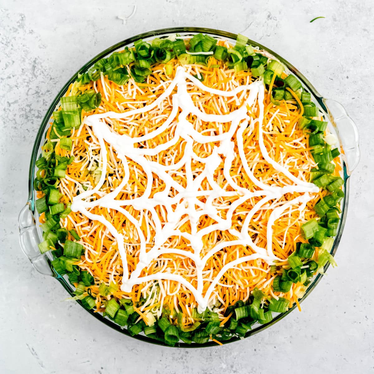 Sour cream spiderweb on top of a pan of taco dip