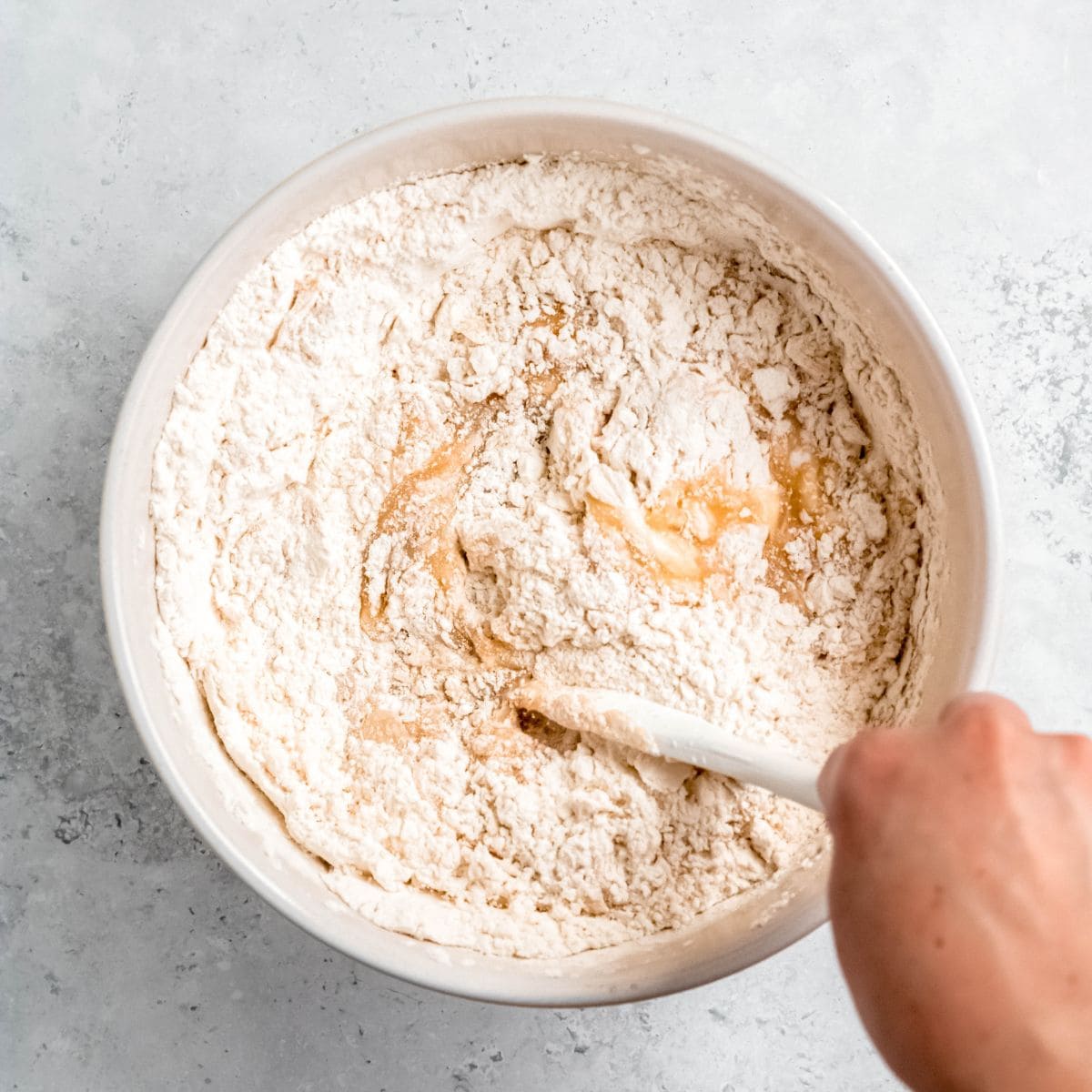 A hand stirs together muffin batter in a white bowl.