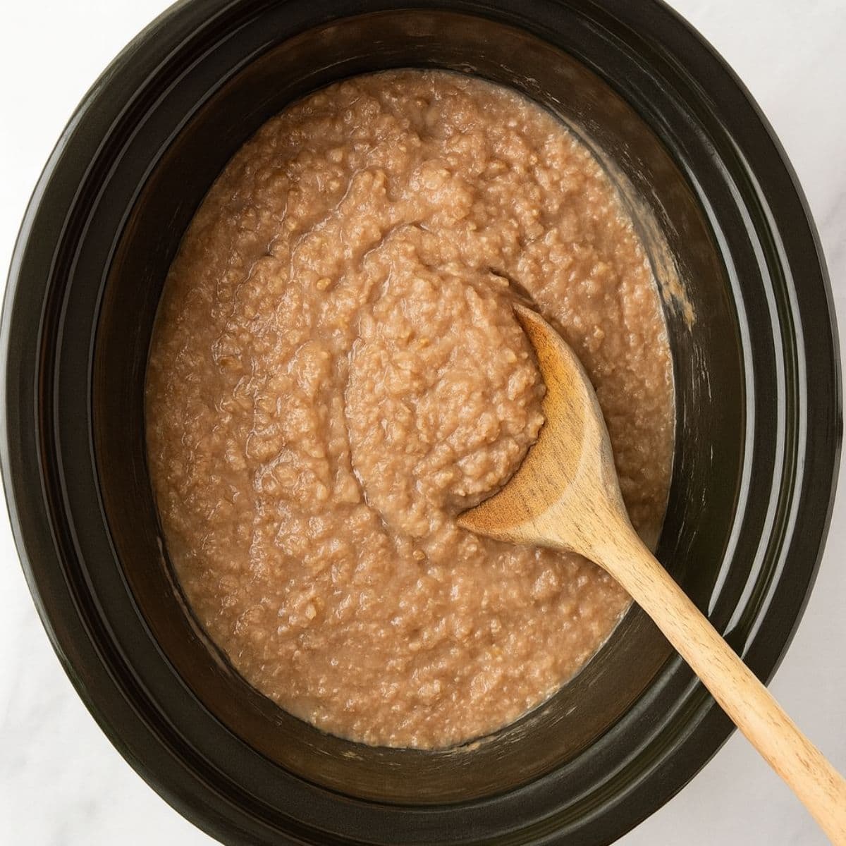A wooden spoon stirs steel cut oatmeal in a slow cooker.