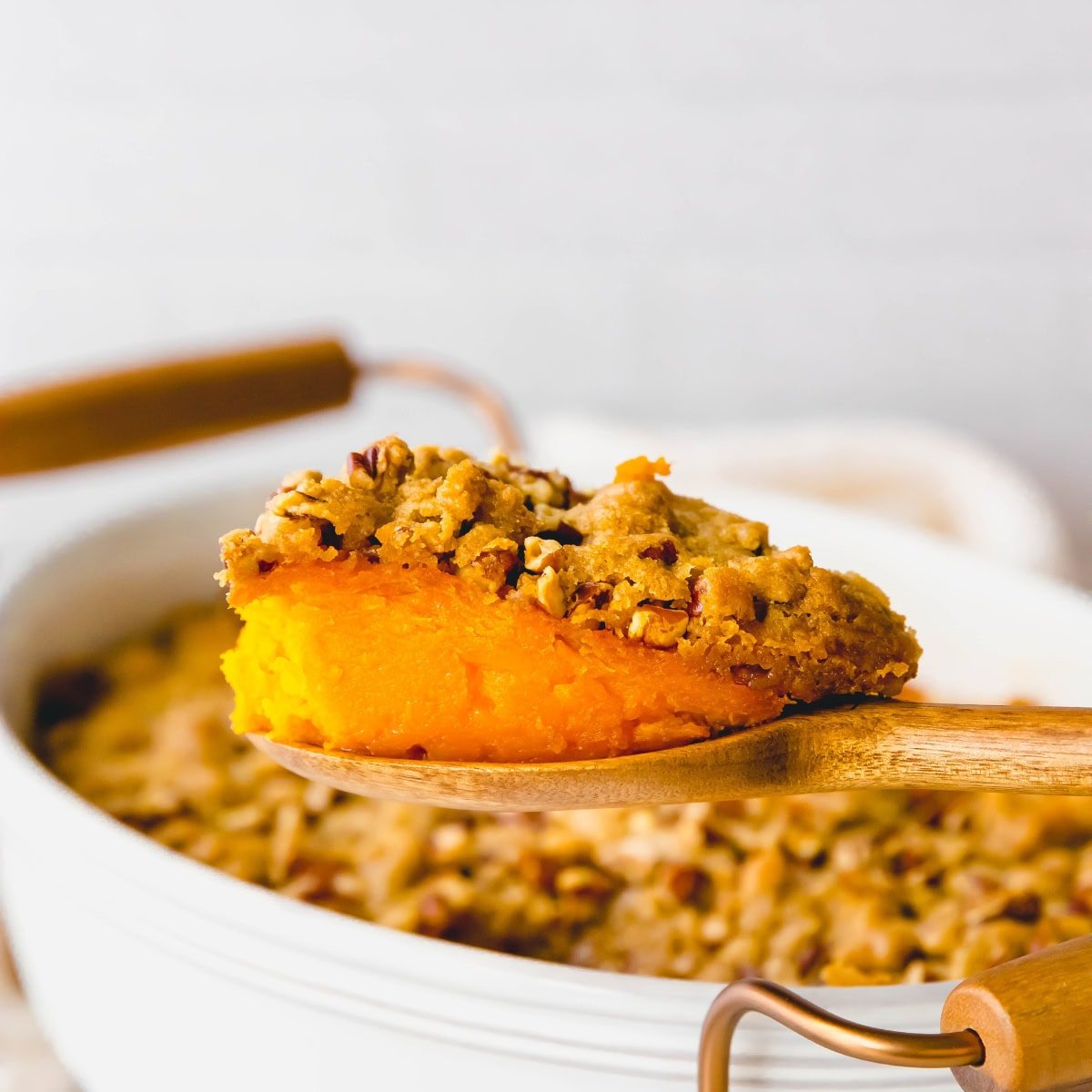 A spoon scoops out some sweet potato casserole from a baking dish