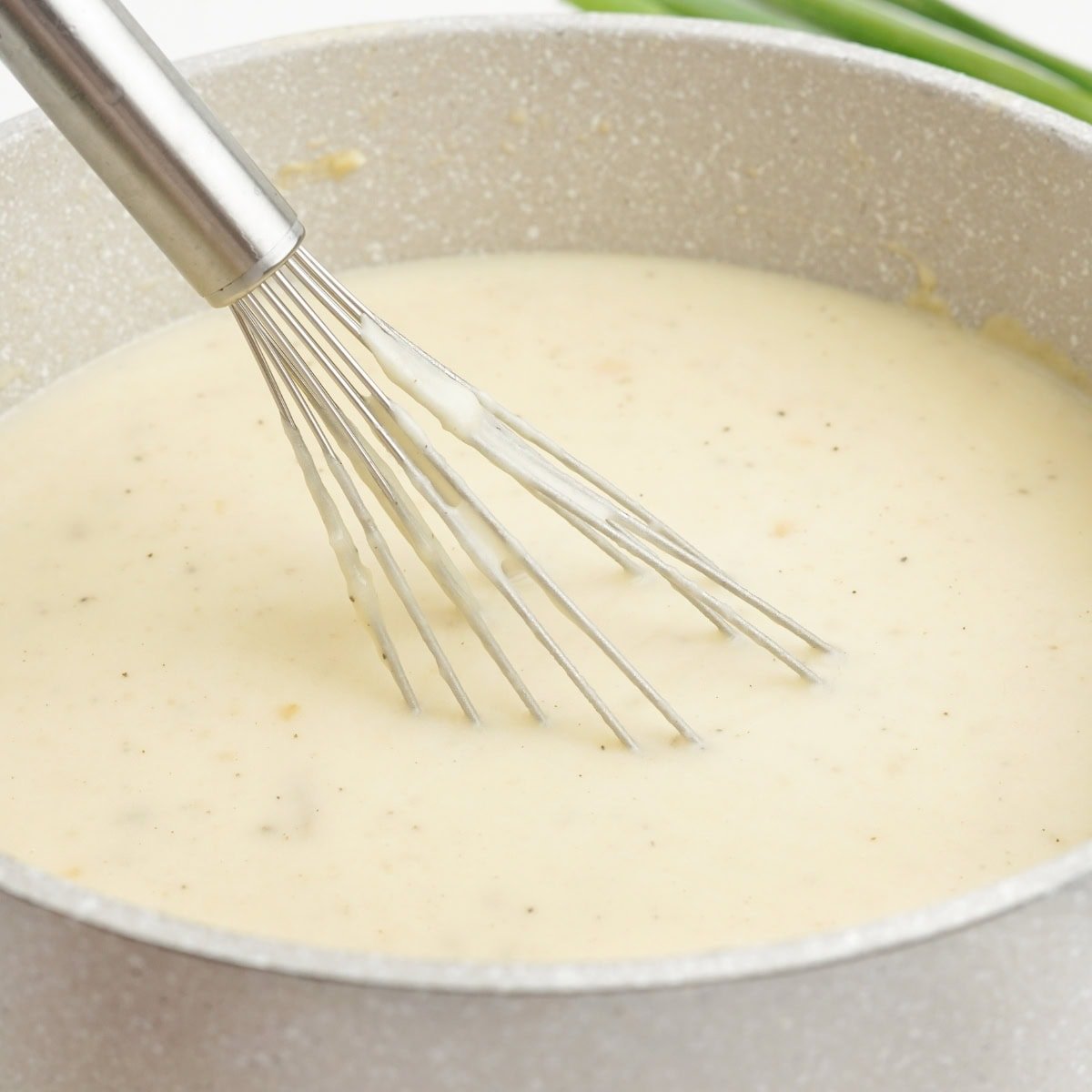 A whisk in a pot of mashed potato soup.