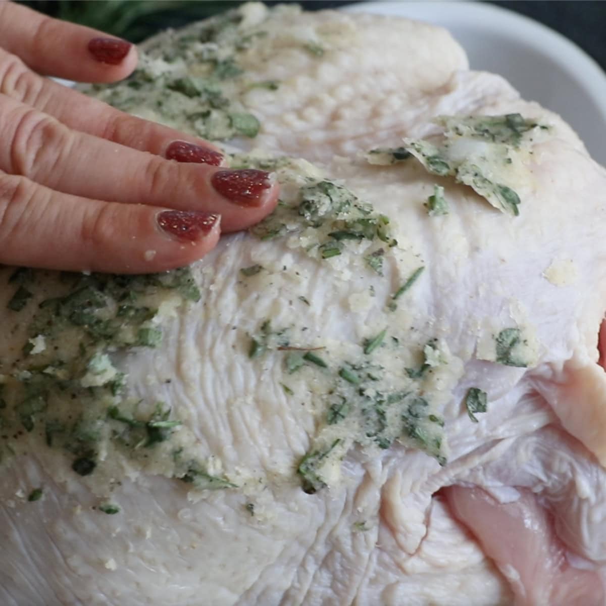 Hands rub seasoning on a raw turkey breast.
