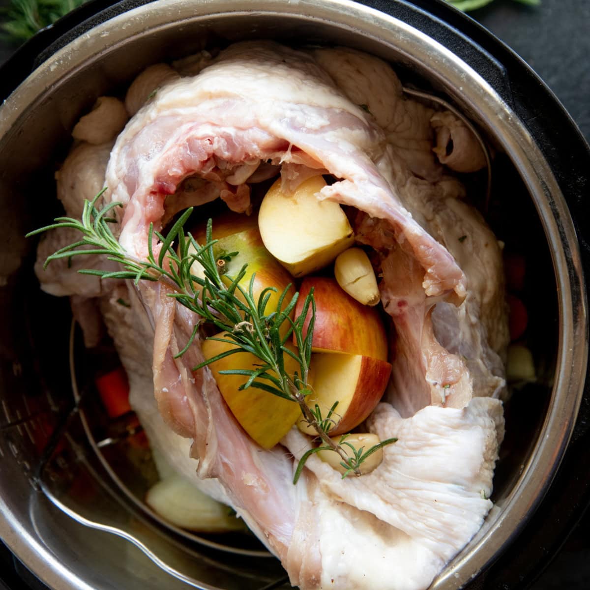 Raw turkey breast in the Instant Pot, stuffed with apples, vegetables, and garlic.