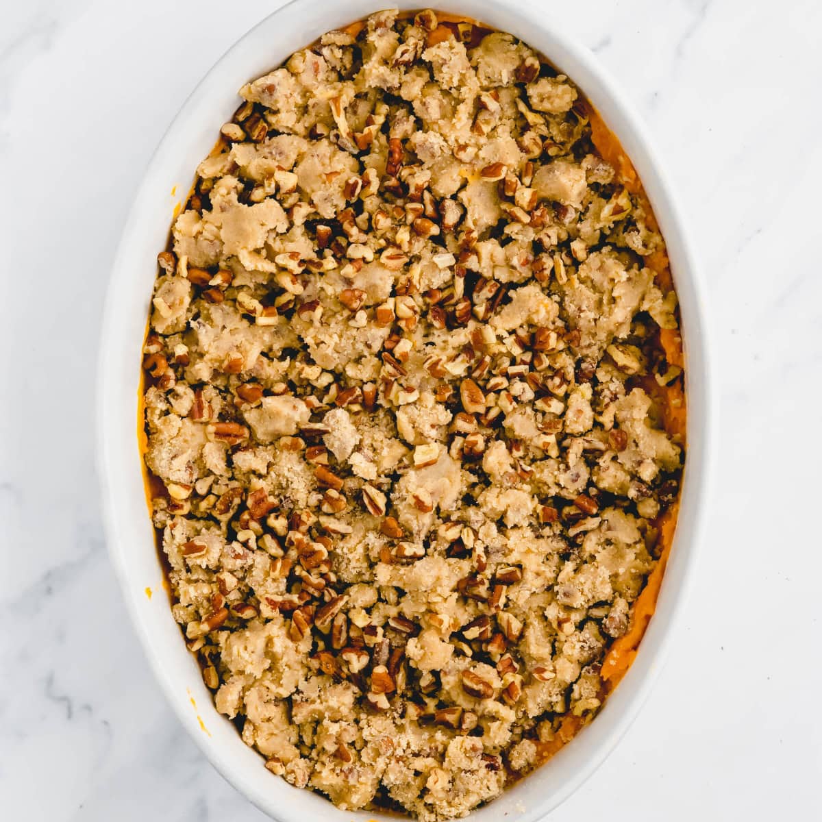 Unbaked sweet potato casserole with pecans in a white casserole dish.