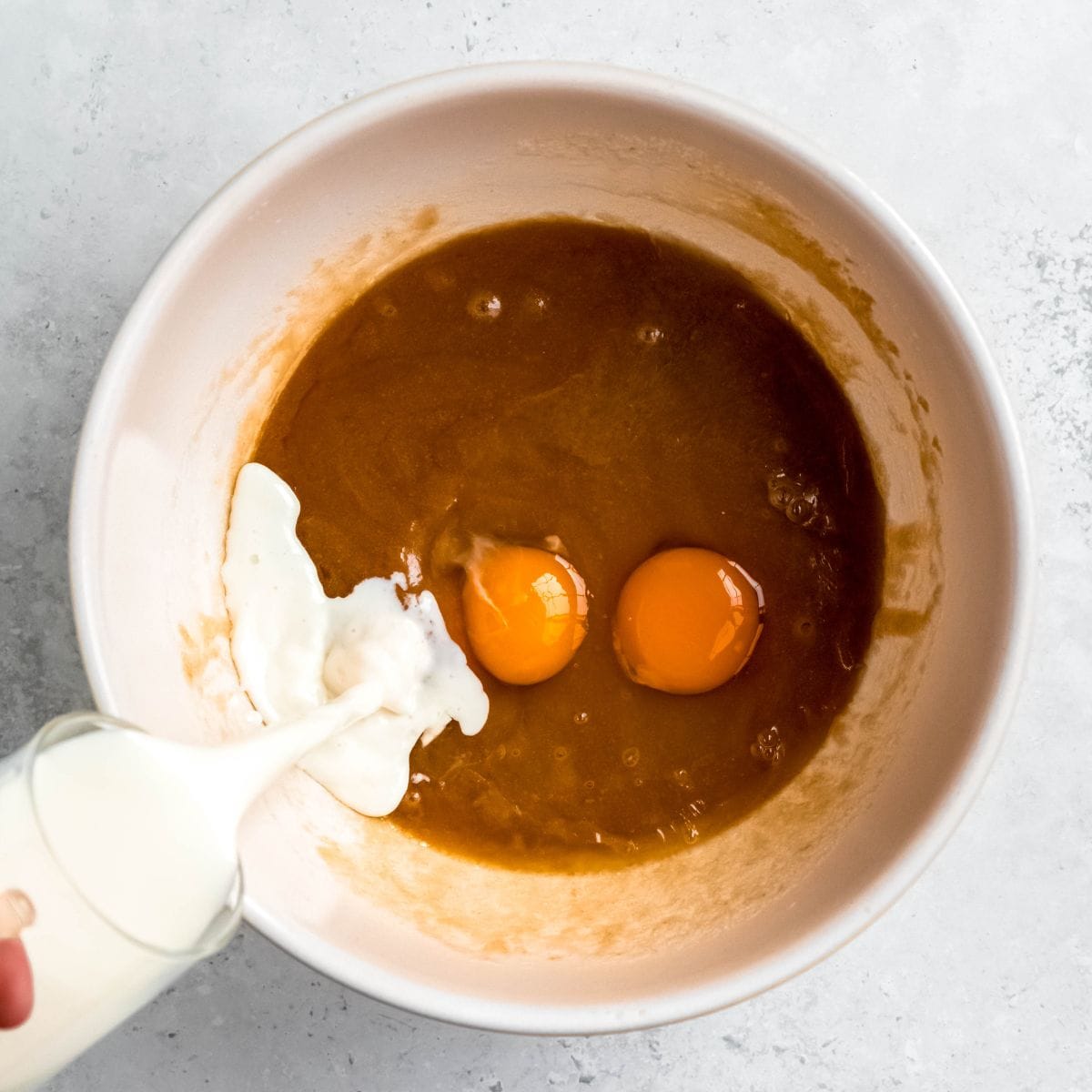Wet ingredients for muffins in a white mixing bowl on a marbled counter.