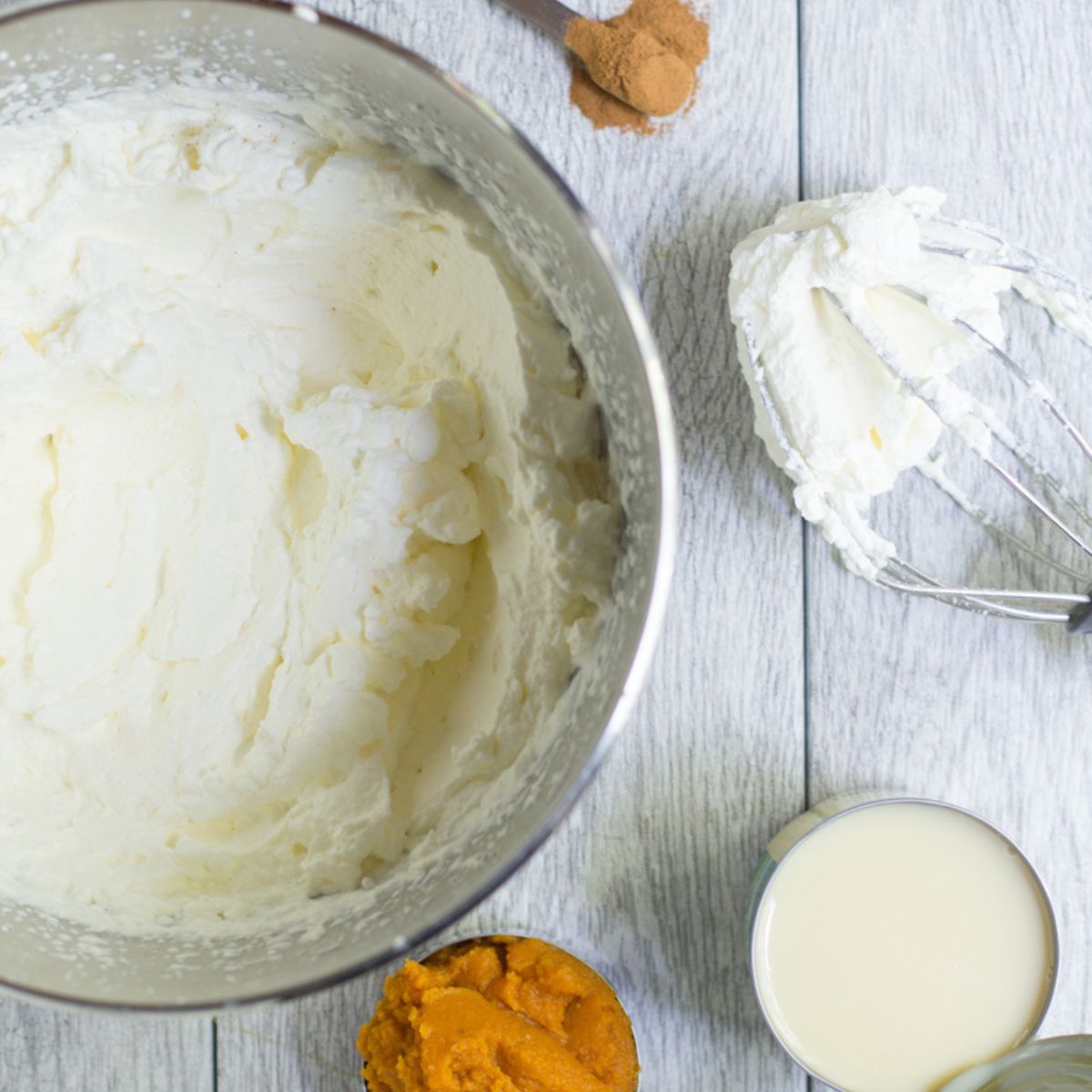 A whisk attachment lays next to a bowl with whipped cream